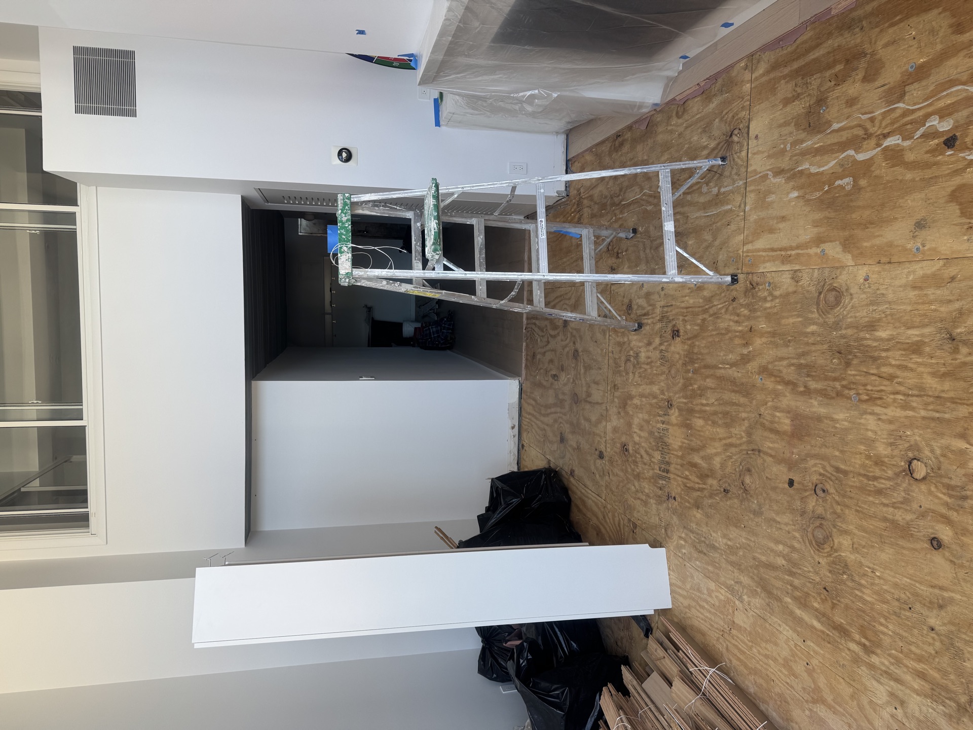 Unfinished wall with exposed plywood and trim stock leaning against framed opening