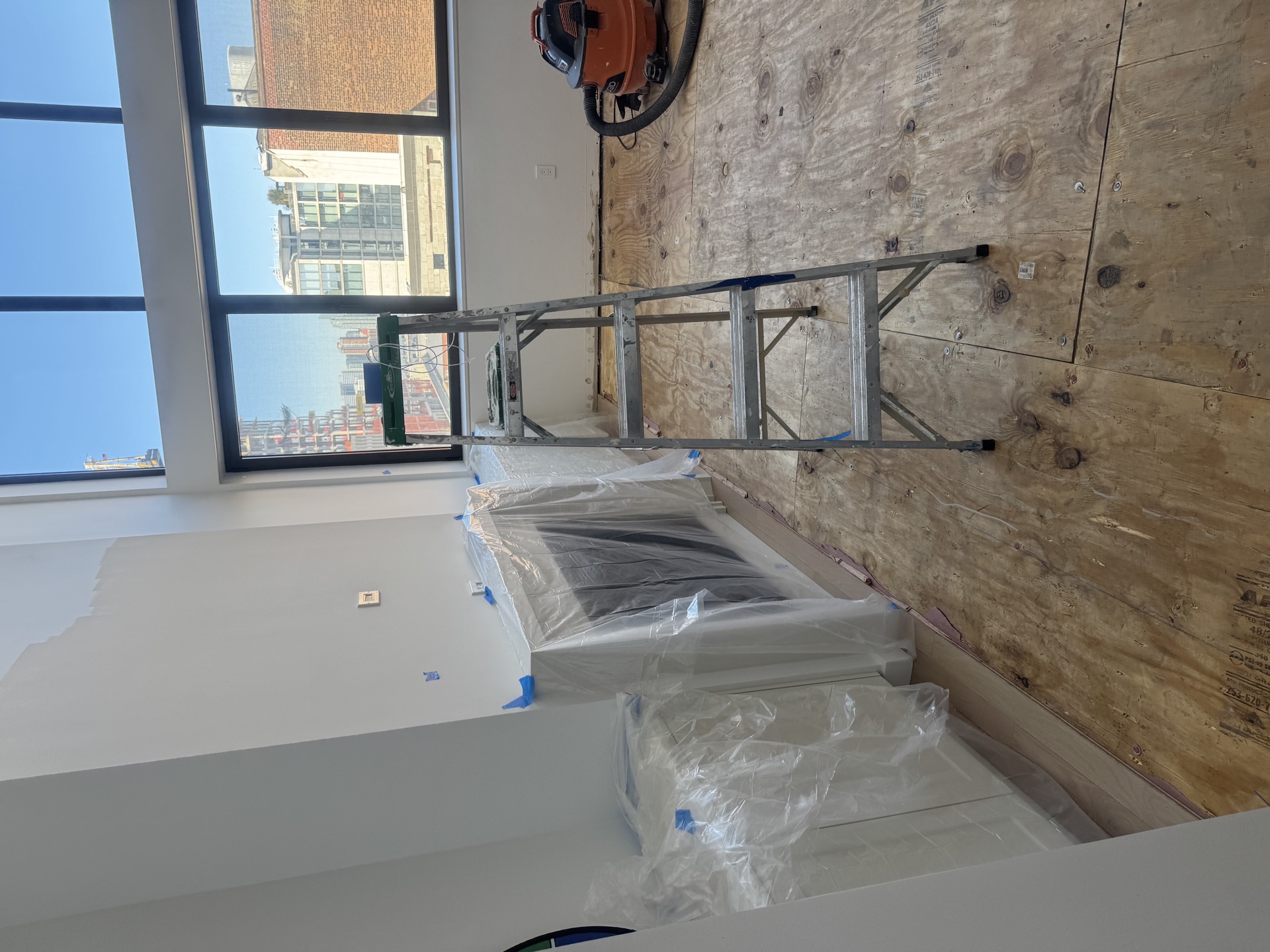 Room mid-build with plywood wall and plastic-wrapped supplies