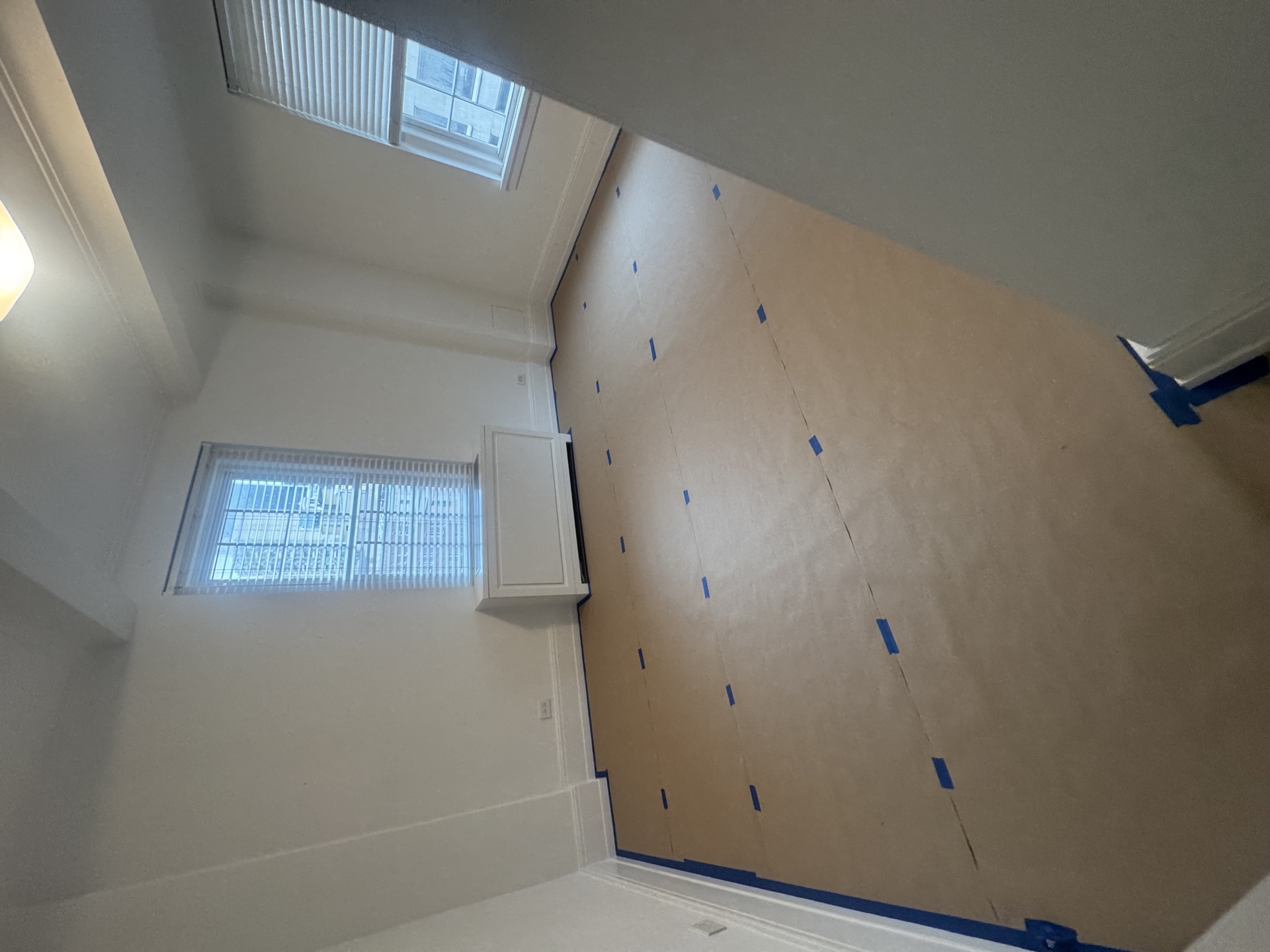 Paint-prep room with kraft paper masking, white baseboards, and double windows