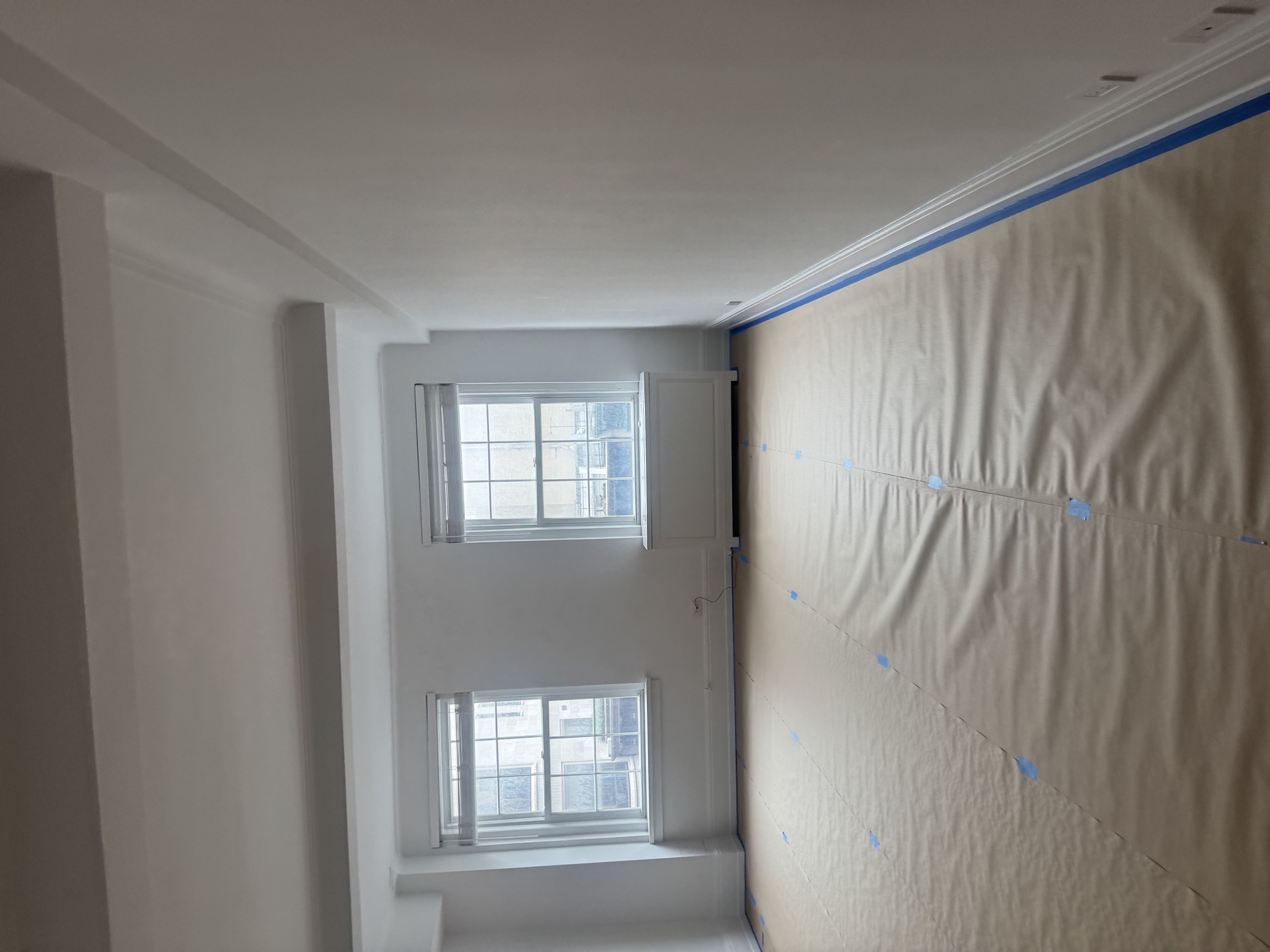 Paint-prep interior with masked walls, crown molding, and mullioned windows
