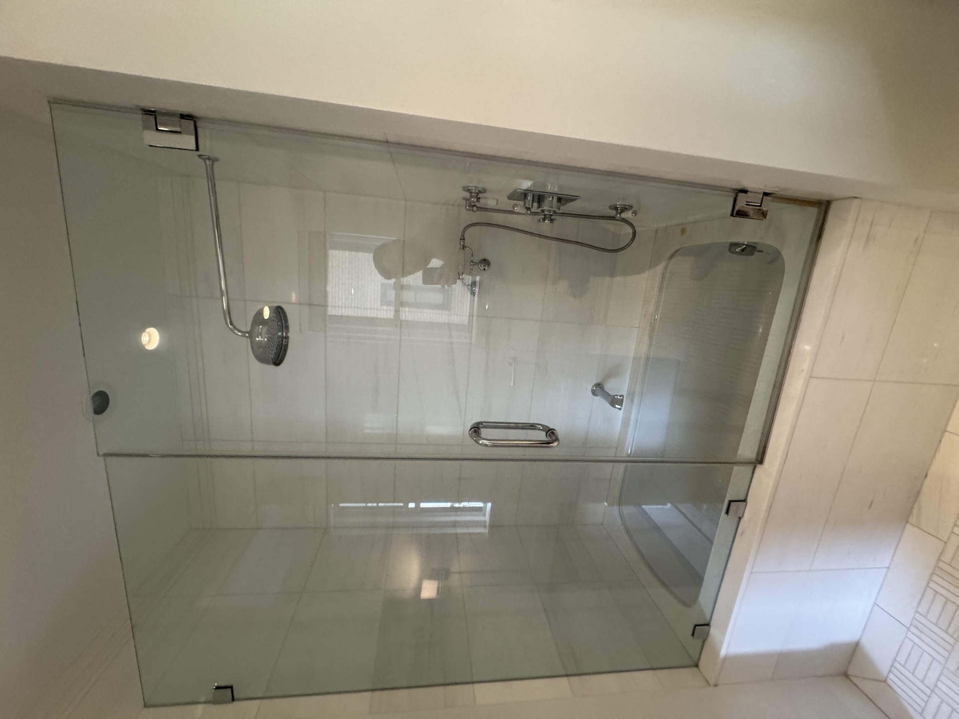 Frameless glass walk-in shower with marble tile walls, rainfall head, and chrome fixtures