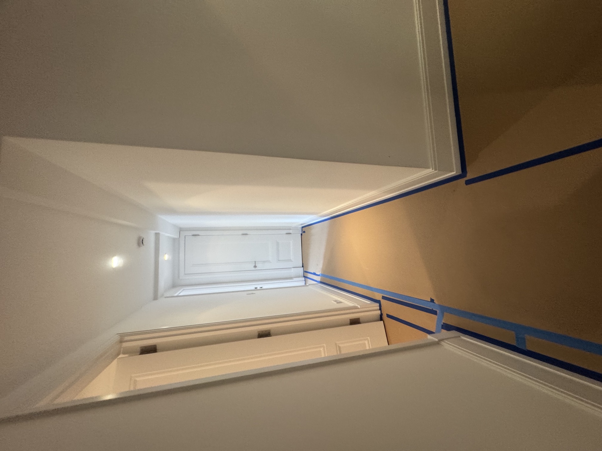 Freshly painted white room with crown molding and blue-tape masking