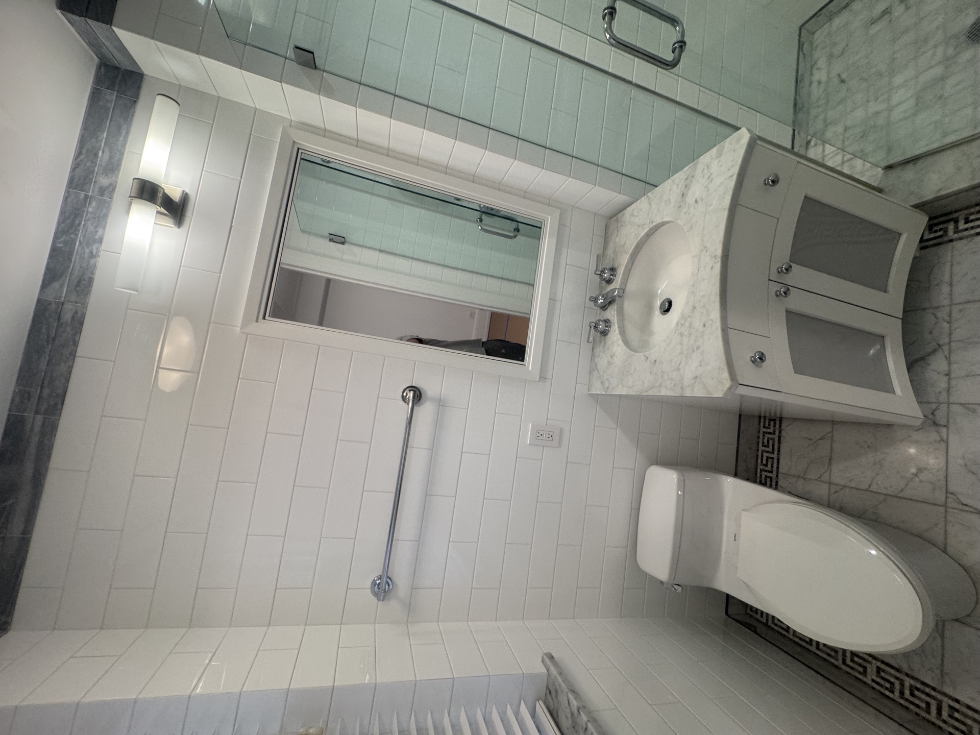 White subway-tiled bathroom with marble vanity, mirrored medicine cabinet, and glass shower