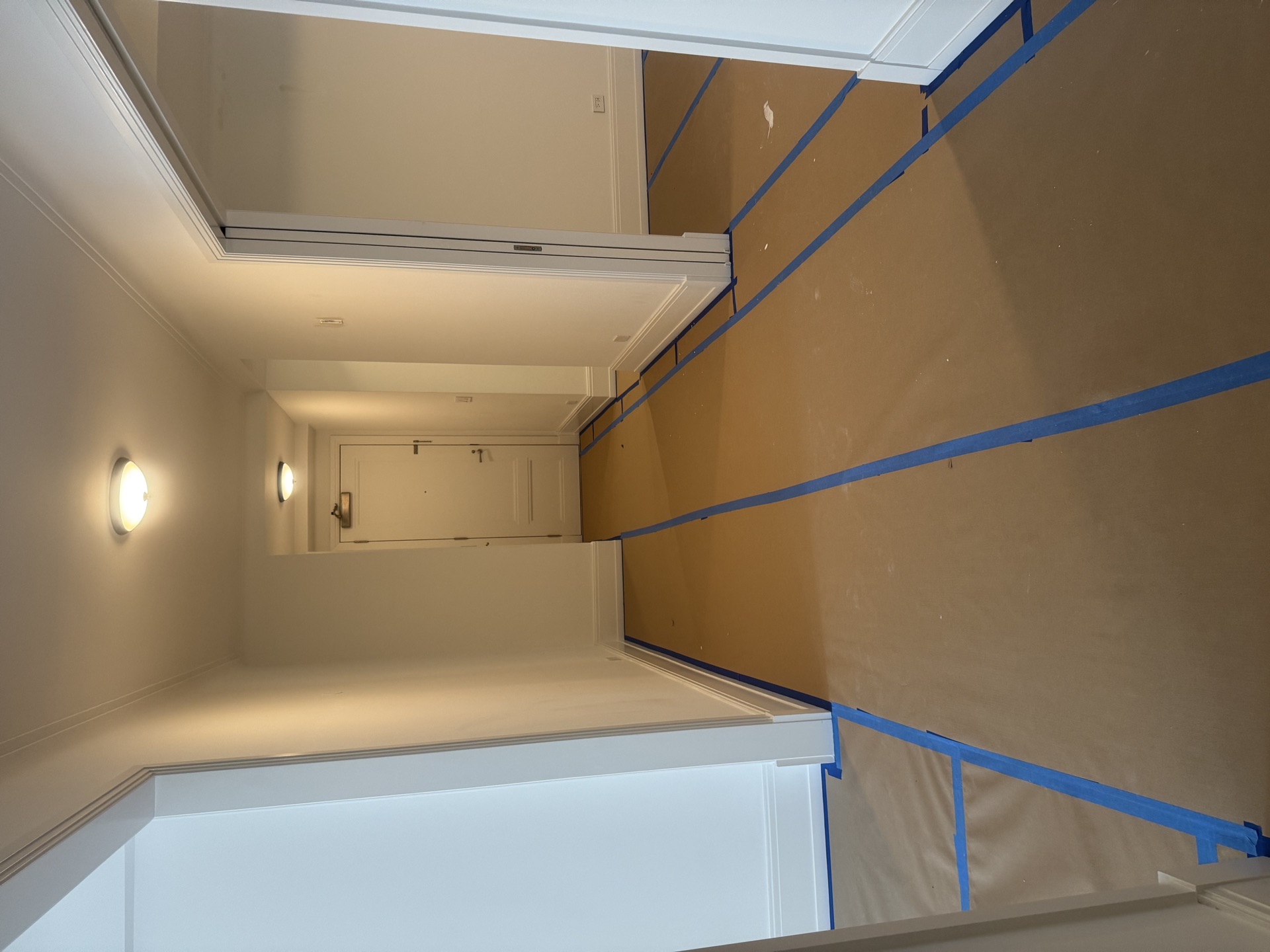 Long painted corridor with crown molding, sconces, and kraft paper masking