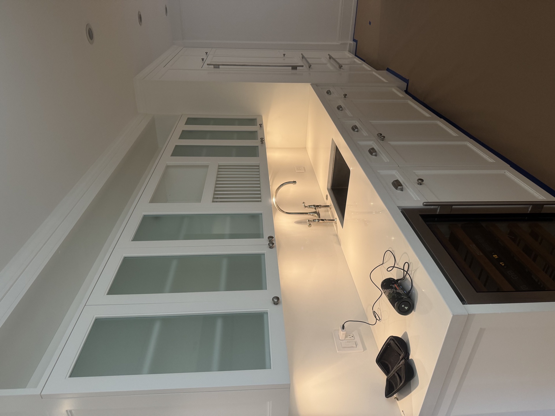 Custom white kitchen with quartz counters, built-in wine fridge, and frosted glass doors
