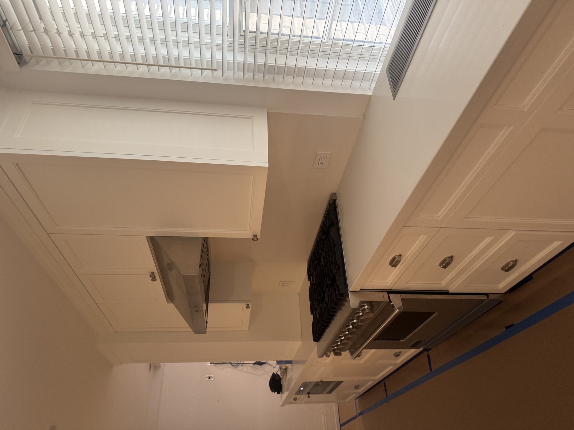Pro-style gas range, stainless hood, and tall white cabinets by bright windows