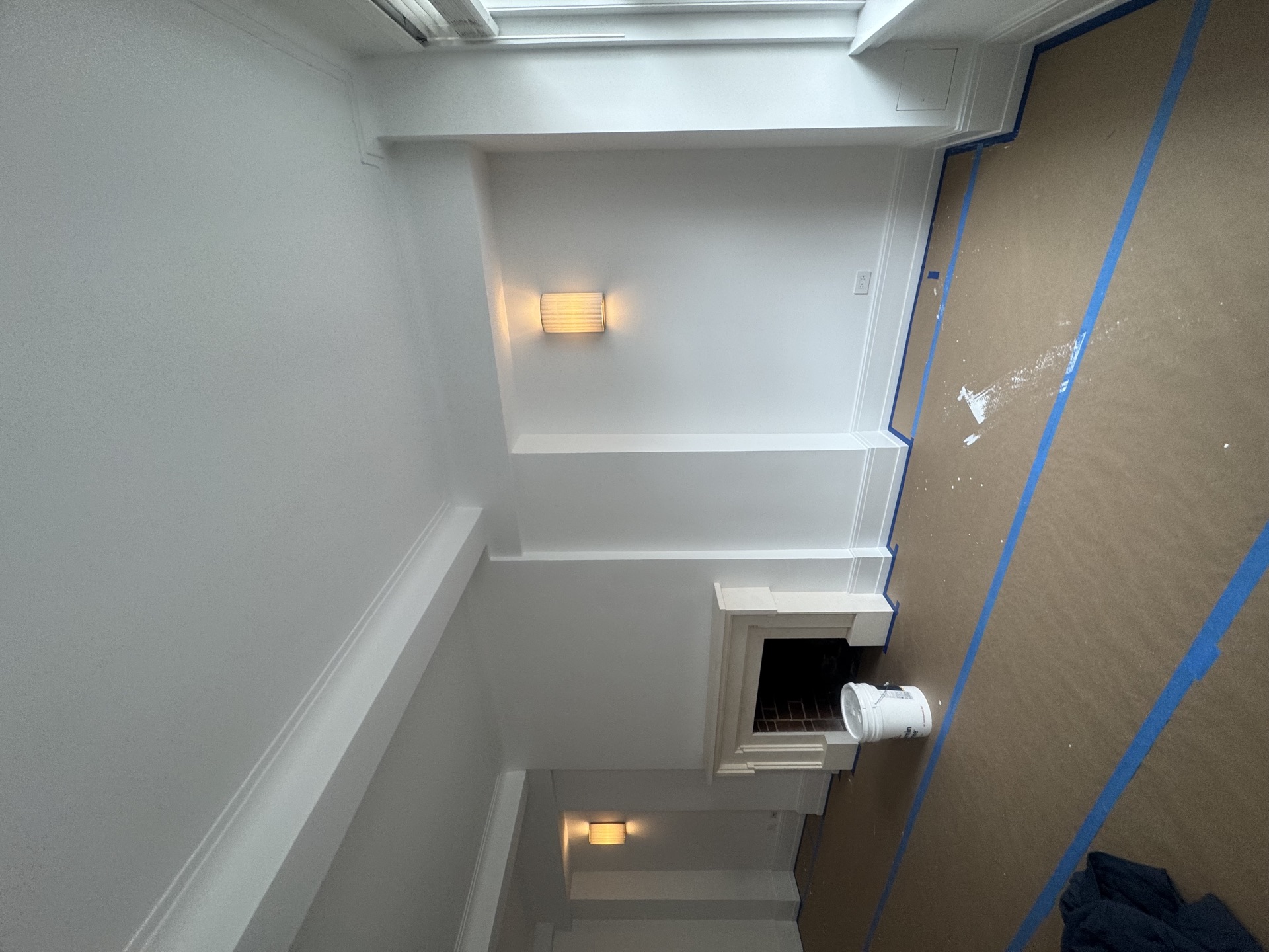 Painted room with wall sconce, fireplace surround, and protective paper