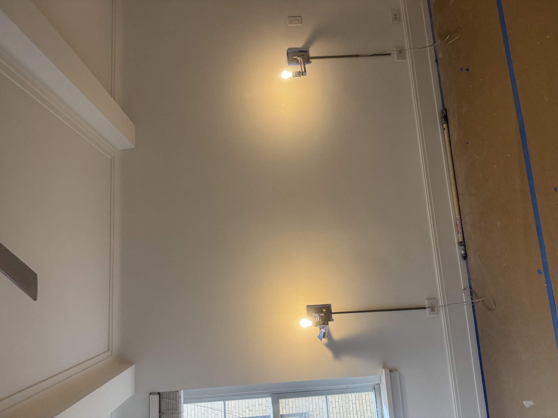 High wall with sconces, blue tape, and protective paper along trim