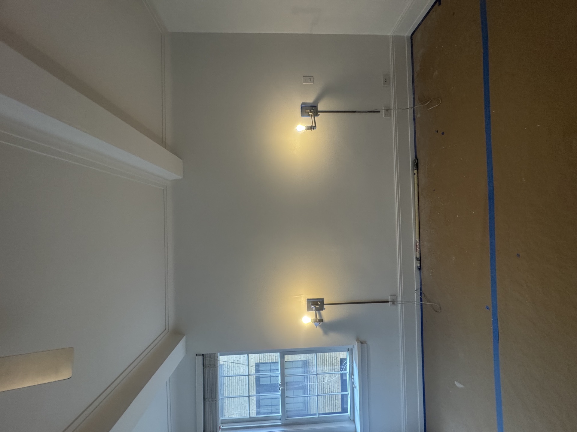 Freshly painted stairwell with sconces, window, and blue tape masking