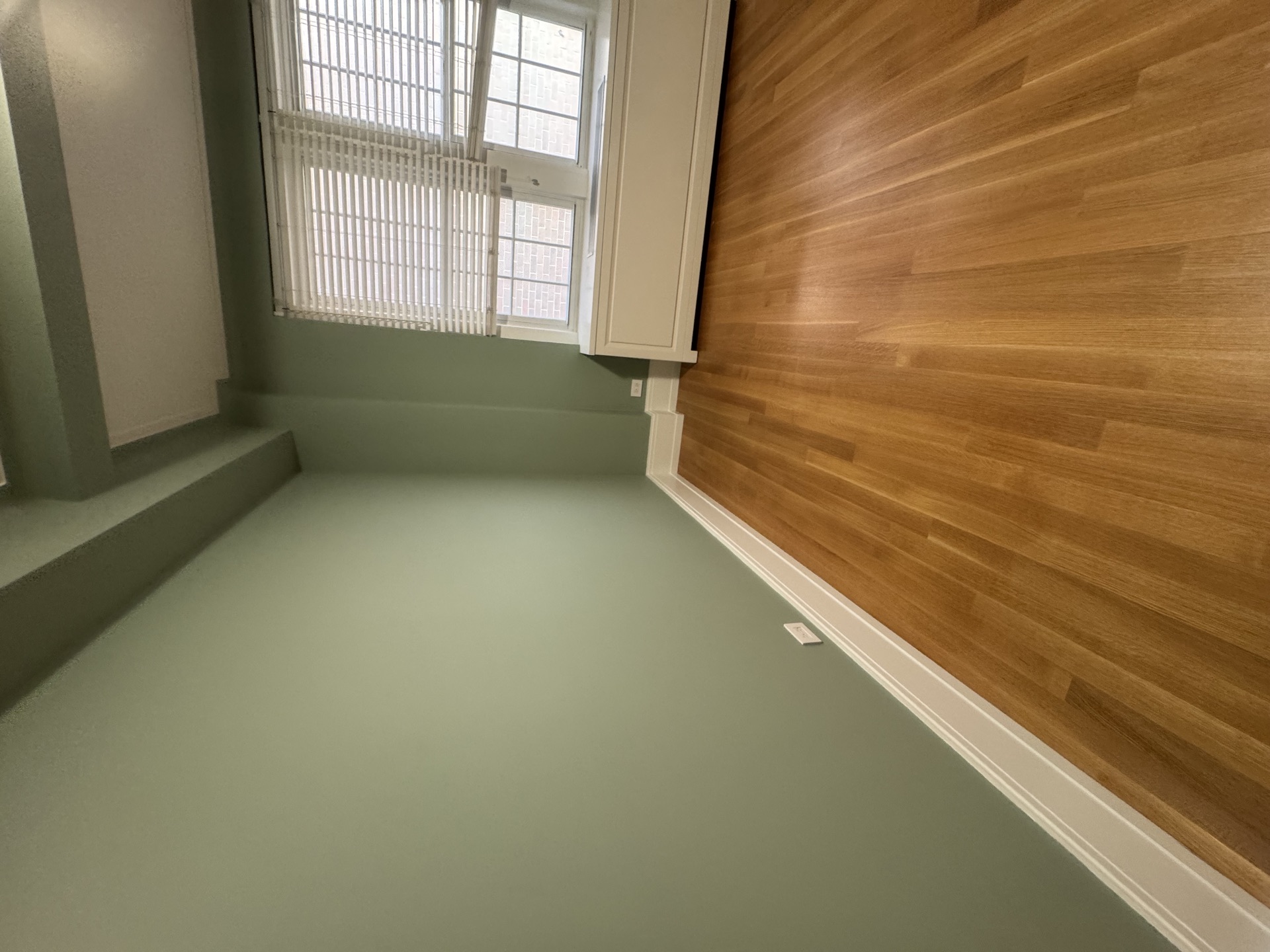 Close-up of hardwood meeting white baseboard in a sage green room