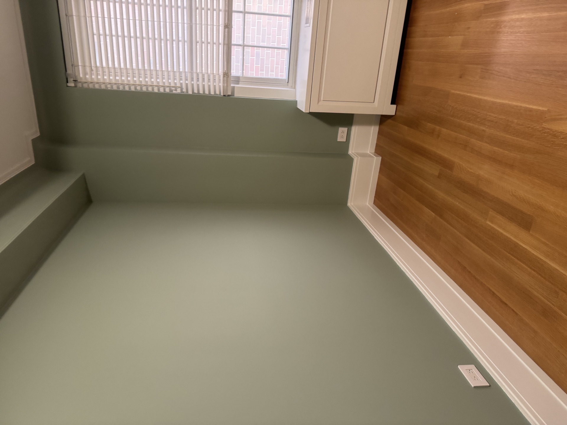 Low-angle shot of hardwood floor and baseboard trim against sage green walls
