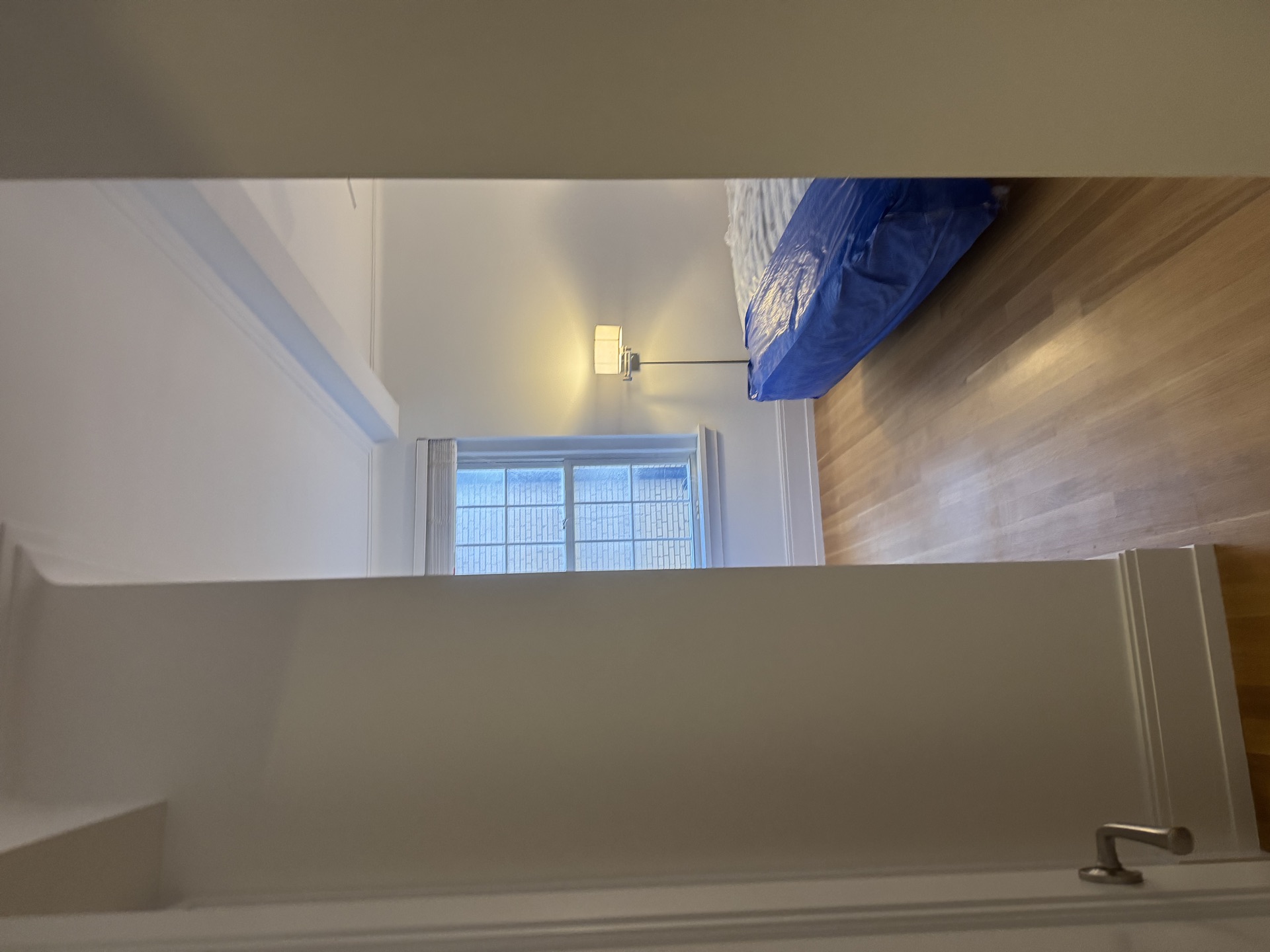 White-walled bedroom with sconce and plastic-covered mattress during renovation