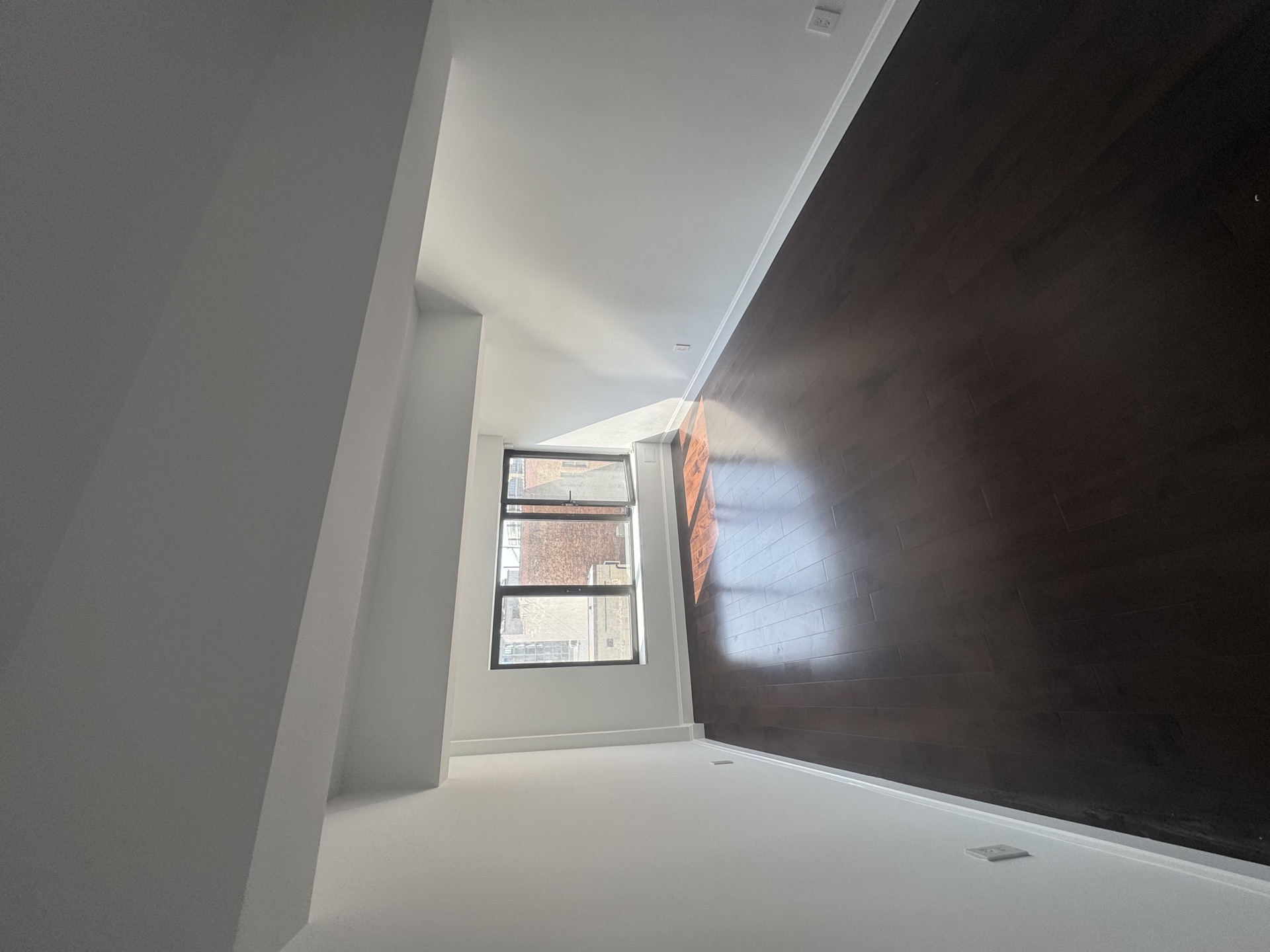 Empty bedroom with dark hardwood, white walls, and a black-framed window