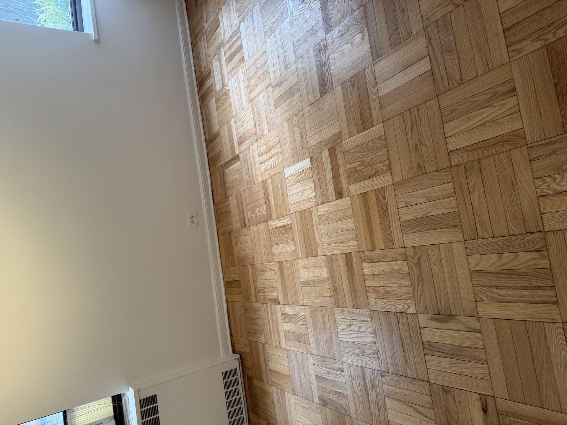 Close-up of refinished parquet block hardwood next to white baseboard