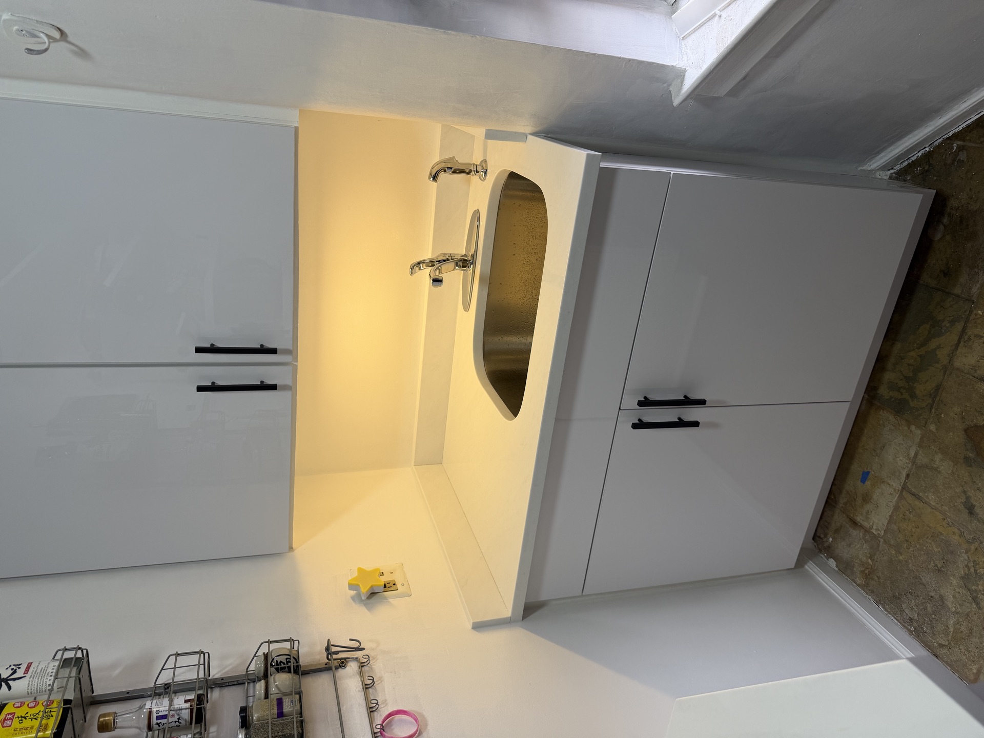Built-in stainless sink niche with wall-mount faucet flanked by glossy white cabinets