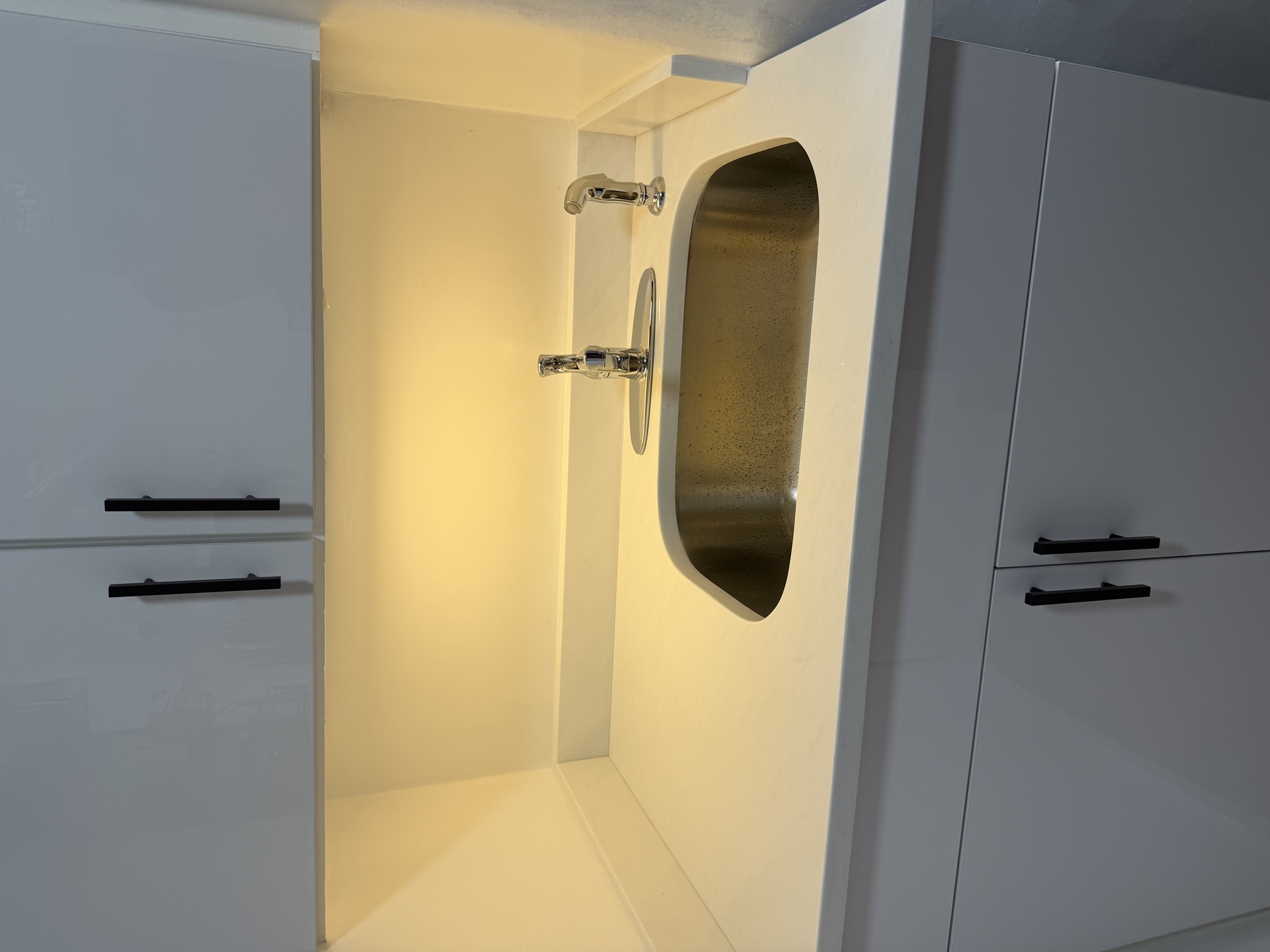 Recessed stainless sink with chrome wall-mount faucet between white cabinets